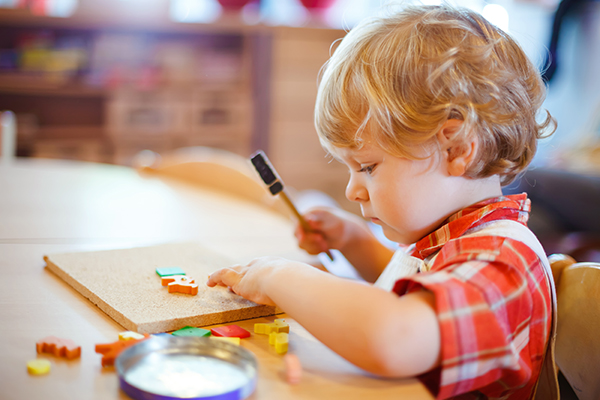 Little cute toddler boy playing with wooden puzzle hammer toys. Happy baby child playing at playschool or kindergarten. children at day care doing activity.